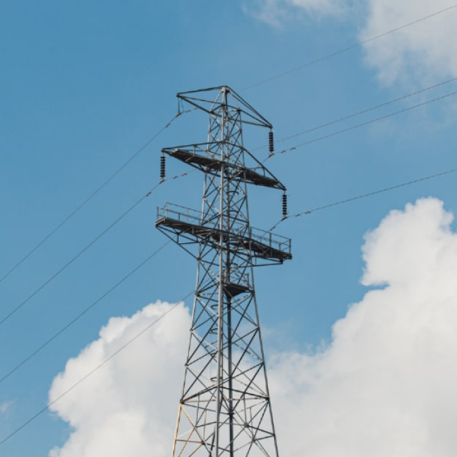 Tall metal power transmission tower with power lines against a blue sky with white clouds
